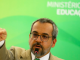 Na foto com fundo verde, o Ministro da Educação Abraham Weintraub fala em frente ao microfone e aponta para frente com o dedo indicador.