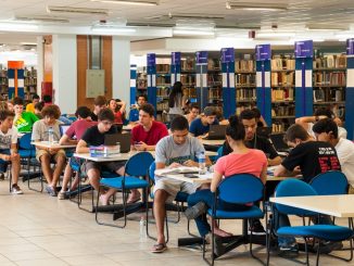 Cerca de dez mesas da Biblioteca Universitária (BU) da UFSC com alunos estudando em livros, cadernos e notebooks.