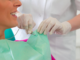 imagem de consultório odontológico, dentista com luvas brancas prende o babeiro na paciente para iniciar o atendimento